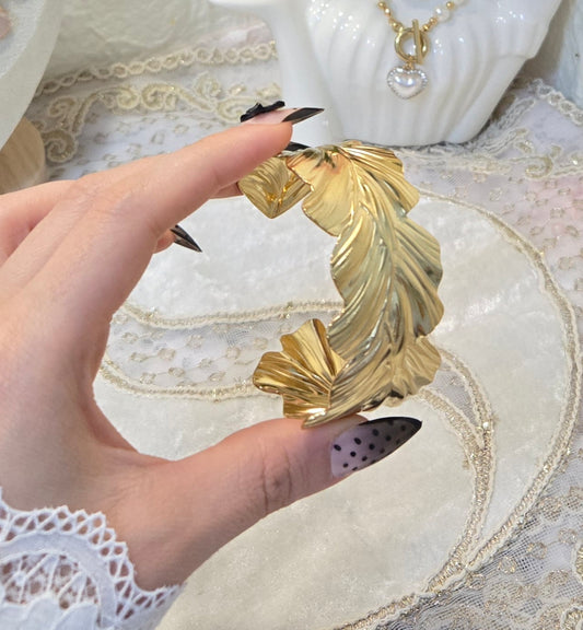 Ein eleganter, goldfarbener Armreif in Form von filigranen Blättern.
